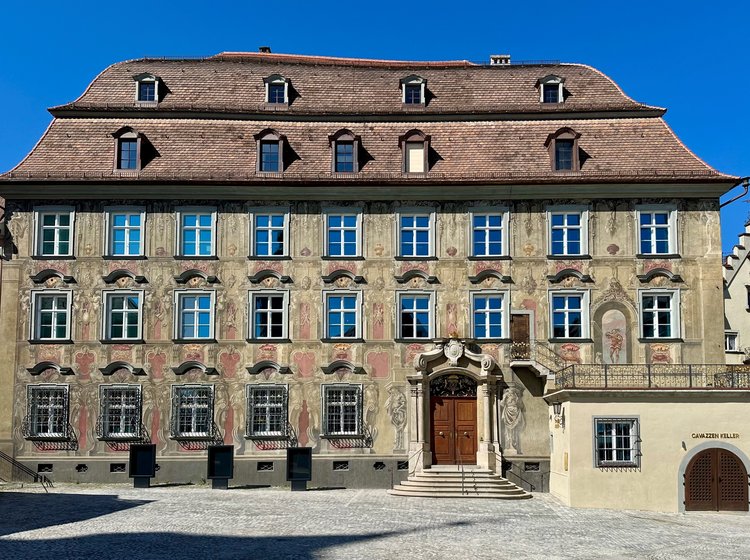 Historisches Museum Cavazzen in Lindau von außen mit Sandsteinfassade und Ziegeldach vor blauem Himmel.