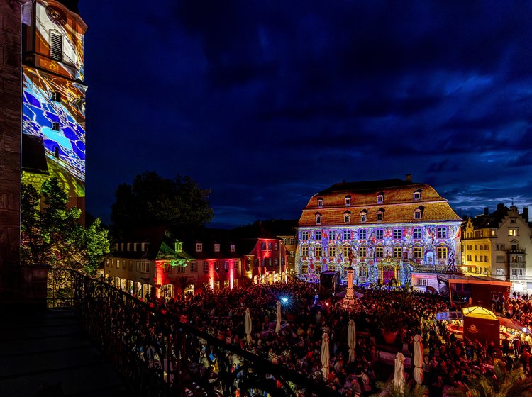 Lindauer Stadtmueum bei Nacht mit farbenfroher Lichtprojektion auf historischen Gebäuden und großer Menschenmenge.