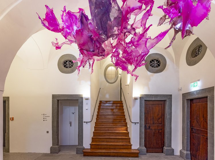 Historisches Treppenhaus im Cavazzen Lindau mit Holzstufen und moderner, pink-violetter Deckeninstallation.