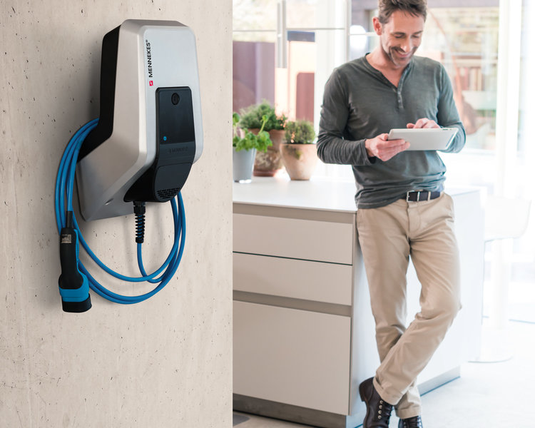 Wallbox an einer Wand im Vordergrund. Im Hintergrund Mann mit Tablet.